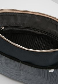 Czarny materiałowy worek z fakturowaną powierzchnią, zamek błyskawiczny oraz gładkie beżowe wnętrze. W środku znajduje się siatkowa kieszeń do organizacji.