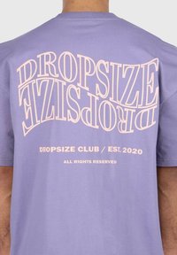 Laventeli puuvillane t-särk, mille seljal on suured, kaardus heledast roosast tekst "DROPSIZE CLUB / EST. 2020", millel on sile tekstuur.