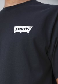 T-shirt en coton noir avec un logo Levi's blanc sur la poitrine. Manches courtes avec un col rond classique. Texture lisse.