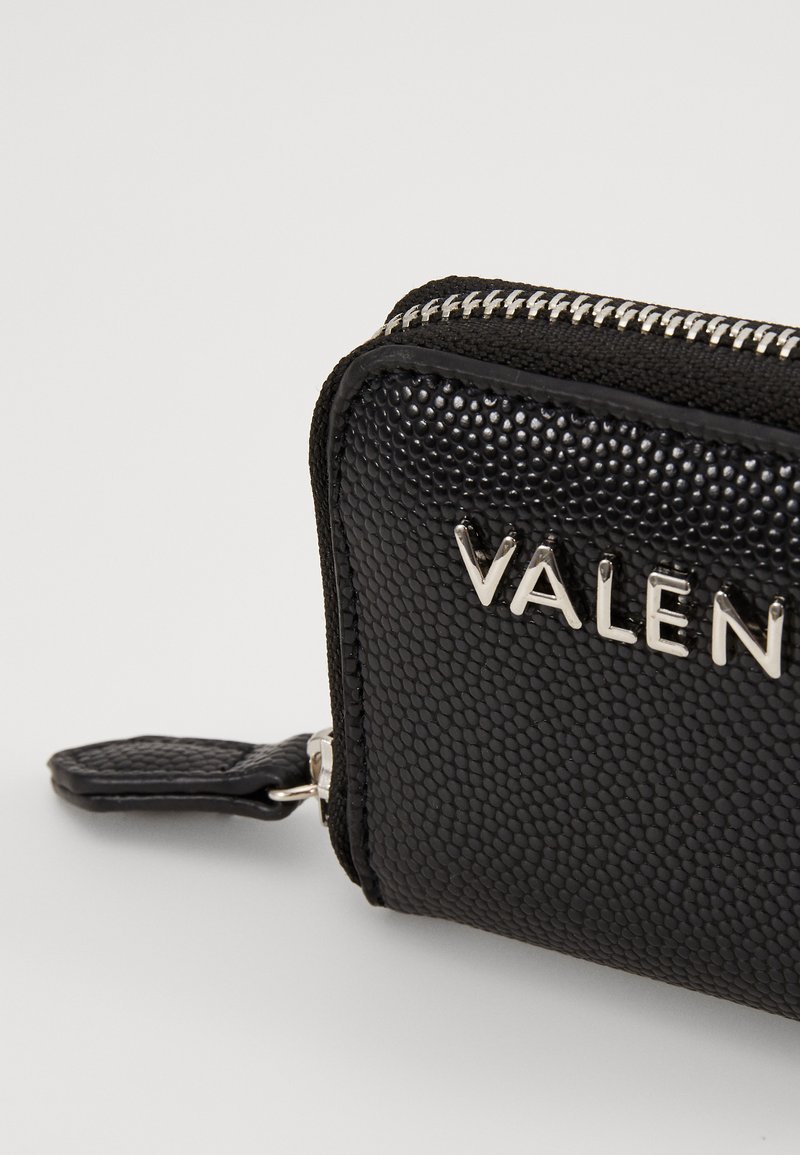 Billetera de cuero negro texturizado con una cremallera plateada y una marca exhibida en el frontal en letras plateadas. Presenta un acabado suave y granuloso.