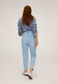 Jasnoniebieskie dżinsy z wysokim stanem i zwężanymi nogawkami, z dwoma tylnymi kieszeniami i efektownym wyblakłym wykończeniem, zestawione z szarym swetrem.