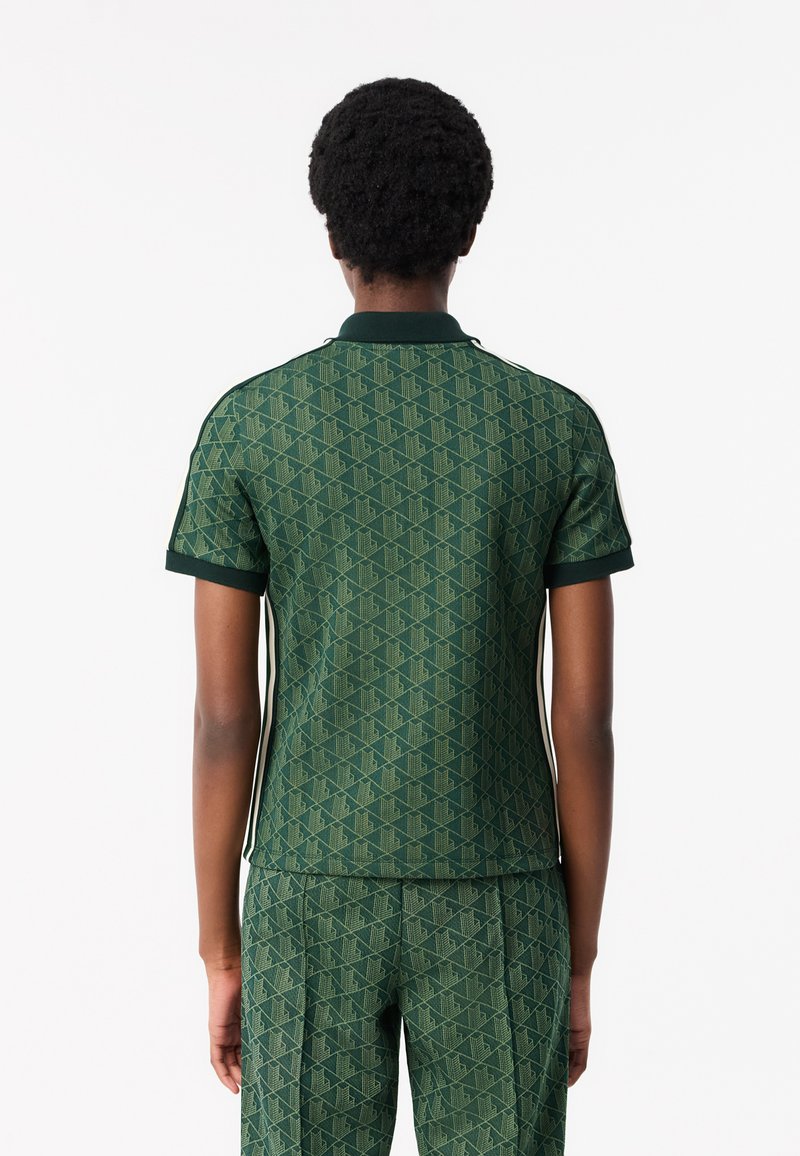 Zielona koszulka polo z wzorem i teksturowanym wykończeniem, z żebrowanym kołnierzykiem i mankietami oraz bocznymi paskami. Przedstawiony widok z tyłu.