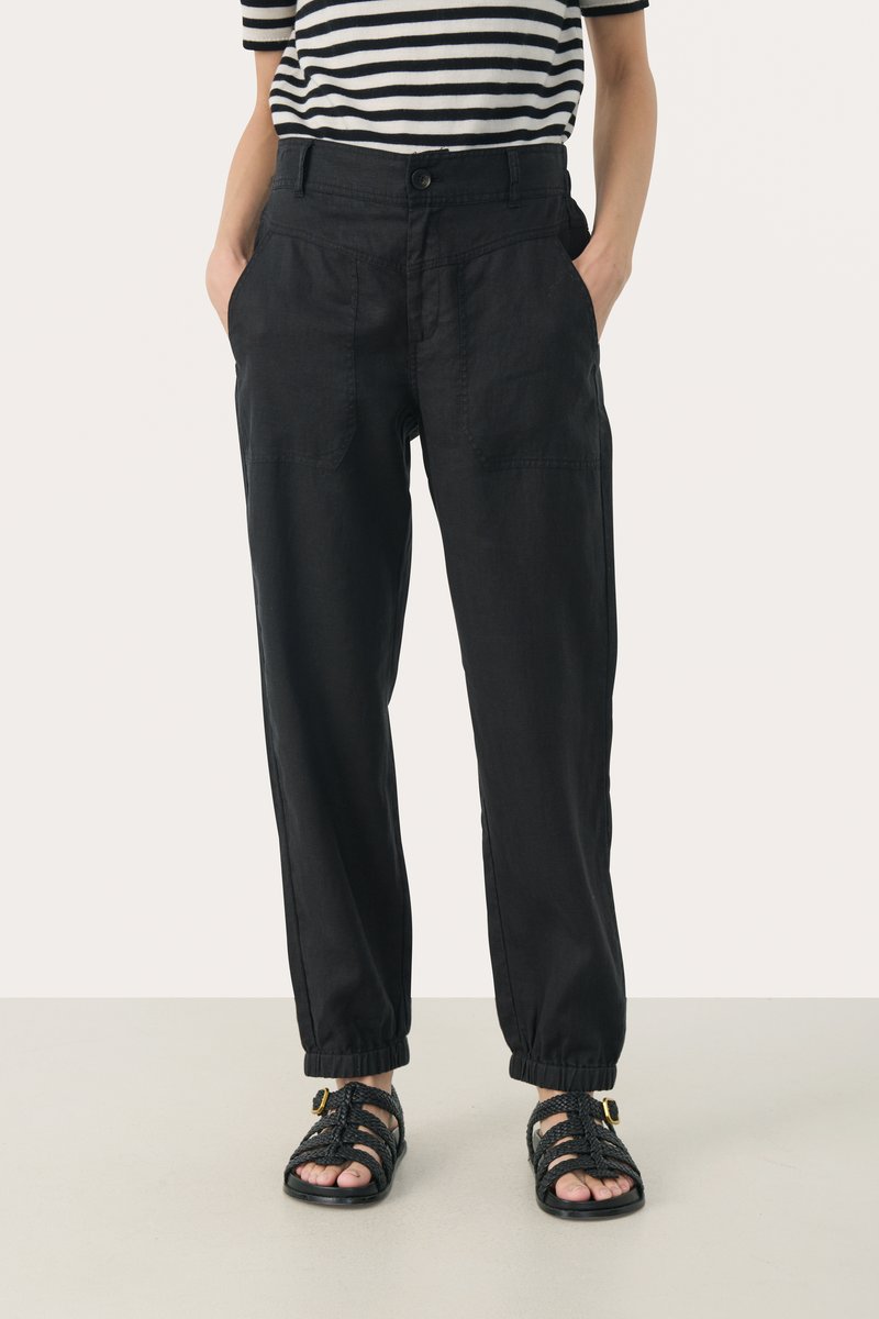 Black, loose-fitting pants made of lightweight fabric, featuring front pockets and elastic cuffs, paired with strappy black sandals.