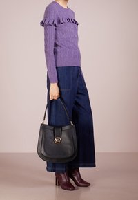 Fioletowy sweter w gruby splot z falbanianym dekoltem, zestawiony z ciemnymi szerokimi spodniami jeansowymi oraz czarną skórzaną torebką z złotym akcentem w formie logo.