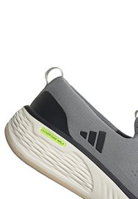 Zapatilla deportiva sin cordones gris y negra con suela blanca texturizada y etiqueta verde neón "Cloudfoam Walk" en el lateral del talón.