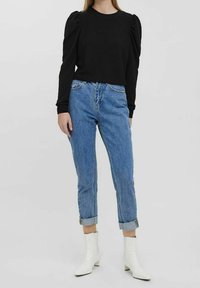 Top negro texturizado de manga larga con hombreras abullonadas, combinado con vaqueros azul claro y botines blancos hasta el tobillo. Corte recto con puños remangados.