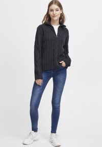 Dark gray cable-knit pullover with a zip collar, ribbed texture, and long sleeves, paired with blue skinny jeans and white sneakers.