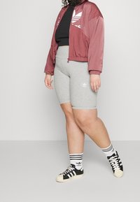 Mörkröd träningsjacka med vit logotyp, svart crop top, grå cykelshorts, svart och vit sneakers, och randiga strumpor. Avslappnad sportkläder.