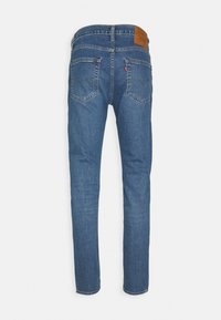 Blå denimjeans med rak benmodell, utrustade med två bakfickor, en brun läderlapp på midjebandet och synliga sömdetaljer.