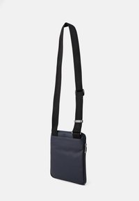 Bolso cruzado azul marino hecho de material suave, con una correa negra ajustable, cierre de cremallera y un diseño rectangular minimalista.