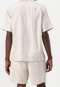Conjunto de camisa de lino de manga corta y pantalones cortos, con rayas verticales en beige y acentos en azul claro, corte relajado, textura visible.