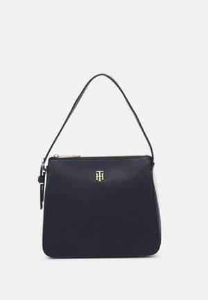 Sac à main en cuir noir avec une seule bandoulière, une fermeture éclair dorée et un petit logo doré centré sur le panneau avant.
