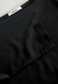 Fekete pamut póló, kerek nyakkivágással és betekintő zsebbel, sima textúrával és finom varrással a széleken.