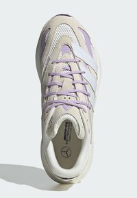 Sneaker w pastelowej kolorystyce, z siateczkowych i zamszowych materiałów, białymi paskami i fioletowymi akcentami. Okrągły kształt z teksturowanymi detalami.