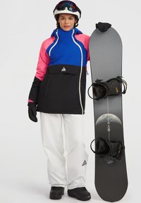 Kleurrijke snowboardjas met blauwe, roze en zwarte delen, gecombineerd met witte sneeuwbroek en zwarte snowboard met maangrafiek.