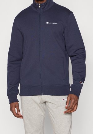 Námořnicky modrá mikina na zip s vysokým límcem, s bílou výšivkou loga na hrudi a manžetě. Měkká směs bavlny.