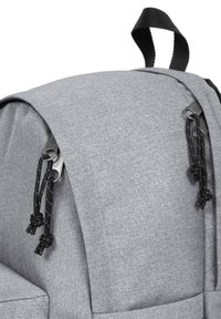 Harmaa kangaskassi, jossa on pyöreä yläosa, säädettävä musta naru ja metalliset vetoketjuakcentit. Kankaan tekstuuri kestävyyden takaamiseksi.