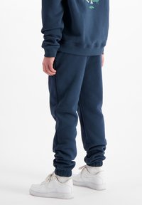 Navyblauwe sweatshirt en bijpassende sweatpants van zachte stof; de broek heeft elastische boorden en een relaxte pasvorm, gedragen met witte sneakers.