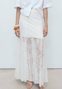 Fustă maxi albă din dantelă, cu modele florale, un design stratificat și o textură semi-transparentă. Purtați-o cu un top alb lejer.