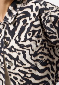 Zwart-wit dierenprint denimjacket met een knoopsluiting, puntige kraag en een voorzak met zichtbare stikdetails.