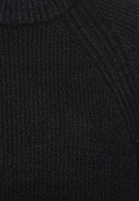 Pull en maille noir avec une texture côtelée, un col rond et des coutures légèrement surélevées le long des épaules.