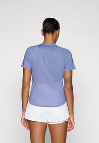 T-shirt de sport bleu clair à manches courtes, avec des panneaux en maille et un ourlet courbé. Présente des rayures verticales d'accent au dos.