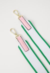 Lanyard con una larga fascia bianca con strisce verdi, dettagli in pelle rosa e clip in metallo dorato alle estremità. Tessuto testurizzato.