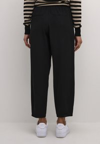 Pantalons noirs à jambe large avec une taille élastique, dotés de deux poches arrière et d'une texture lisse, associés à des baskets blanches.