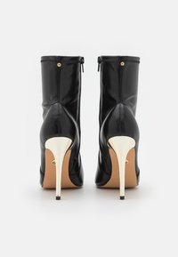 Bottes basses en cuir noir au design élégant, avec un talon stiletto haut en métal doré et une fermeture à glissière latérale.