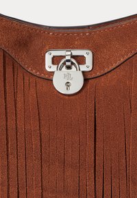 Brown suede bag featuring vertical fringe, a smooth curved top, and a silver-tone lock with brand initials engraved, adding a sleek detail.