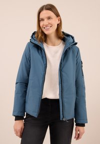 Giacca imbottita blu con cappuccio, zip frontale e tasche laterali. Presenta polsini neri e un esterno liscio e resistente all'acqua.