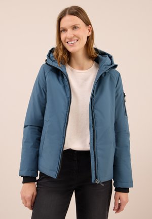 Veste rembourrée bleue avec capuche, fermeture éclair avant et poches latérales. Présente des poignets noirs et un extérieur lisse et résistant à l'eau.