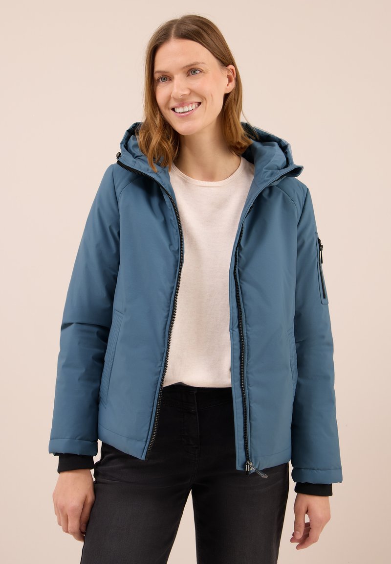 Giacca imbottita blu con cappuccio, zip frontale e tasche laterali. Presenta polsini neri e un esterno liscio e resistente all'acqua.