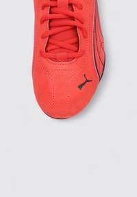 Baskets en daim rouge avec une finition lisse, présentant des accents noirs et une semelle texturée, mettant en avant un design à lacets central et un logo distinct.