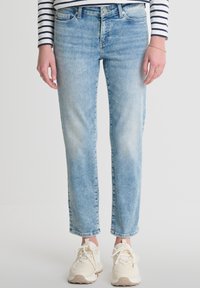 Gai zilu džinsi ar taisnu piegriezumu, ar nelielu nolietojumu un rullētām malām. Apvienoti ar krēmkrāsas kedām un svītrainu augšdaļu.