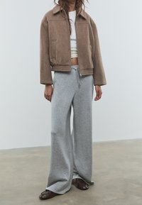 Braune, kurze Jacke aus weichem Stoff, kombiniert mit grauen Sweatpants mit weitem Bein. Verfügt über einen elastischen Bund und Kordelzug. Braune Schuhe vervollständigen das Outfit.