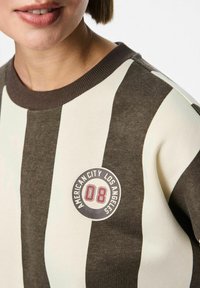 Maglione a righe marroni e crema con un logo tondo che mostra "American City Los Angeles" e il numero "08". Collo a costine.