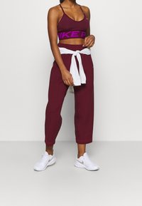 Burgundy sports bra with a purple logo, paired with matching cropped sweatpants and a white tied sweatshirt, completed with white athletic shoes.