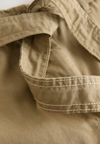 Gros plan sur un tissu beige avec des coutures détaillées et des coutures superposées, mettant en valeur la texture et la fabrication du matériau.