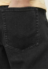 Svarta denimjeans med en bakficka som har ett subtilt sömnadsmönster. Tyget har en mjuk, texturerad yta med synlig väv.