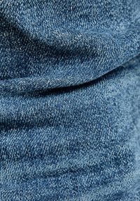 Tejido de denim en tono azul medio con una textura suave, que presenta variaciones sutiles en el tejido y gradientes de color.