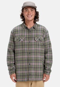 Grünes und rosa kariertes Flanellhemd mit zwei Brusttaschen, Knopfverschluss und langen Ärmeln, das einen strukturierten Stoff zeigt.