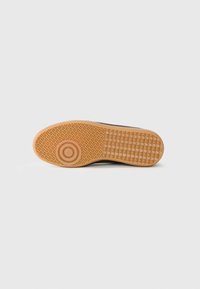 Suola di scarpa con superficie in gomma texturizzata di colore marrone chiaro, caratterizzata da un logo circolare e una presa con motivo per offrire aderenza.