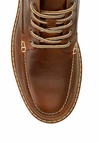 Bottes en cuir marron avec un bout rond, des coutures beige contrastantes et des lacets beige clair. Possède des œillets en métal et une texture lisse.