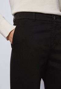Pantalones negros de algodón con una textura suave, que cuentan con un cierre de botón, bolsillos laterales y un diseño ajustado.
