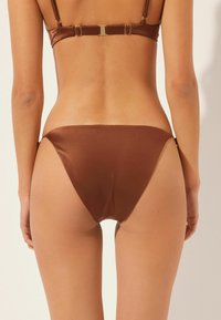 Bruna bikiniunderbyxor tillverkade av slät tyg, med låg midja och minimal täckning, samt diskreta sidoförbindelser.