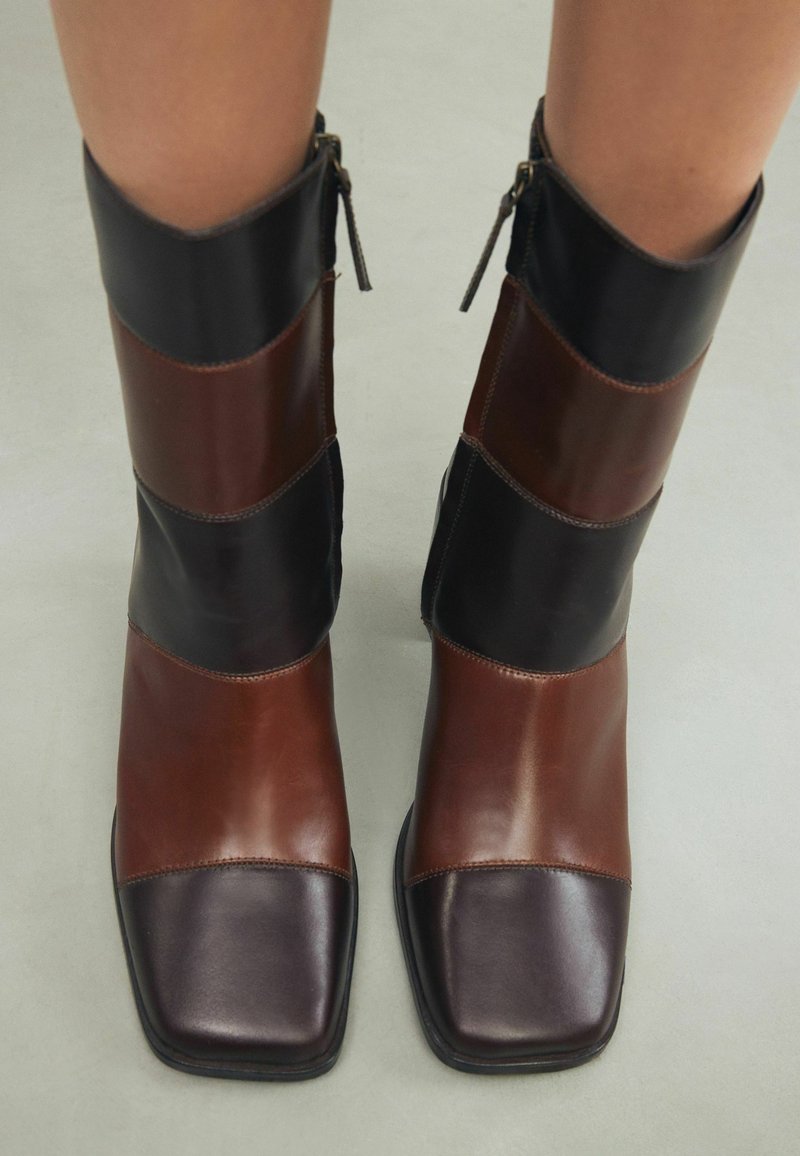 Bottes basses en cuir marron et noir avec un bout carré, présentant un effet color-block vertical et une fermeture éclair latérale pour un enfilage facile.