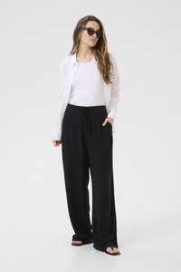 Pantaloni neri a gamba larga con vita elastica e due tasche, abbinati a una canotta bianca e a una leggera camicia bianca. Inclusi occhiali da sole.