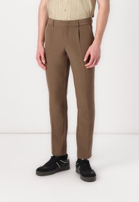 Brown tailored trousers with a smooth texture, slim fit, and pressed creases, paired with black sneakers.
