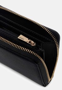 Schwarze Lederbrieftasche mit strukturierter Oberfläche, goldenem Reißverschluss und Metall-Logoschild. Innen mit mehreren Fächern für Karten und Bargeld ausgestattet.